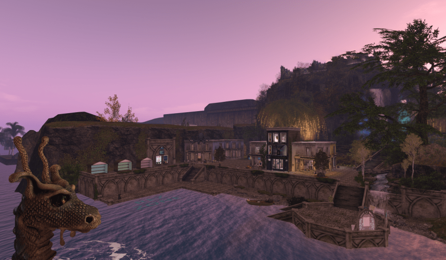 A wide view of Port Emyniad, a seaside arts village on Corsica South Coasters in Second Life. The harbor glows in soft lavender light, with stone buildings, waterfalls, and glowing trees rising beyond the pier — where the sea meets creativity.